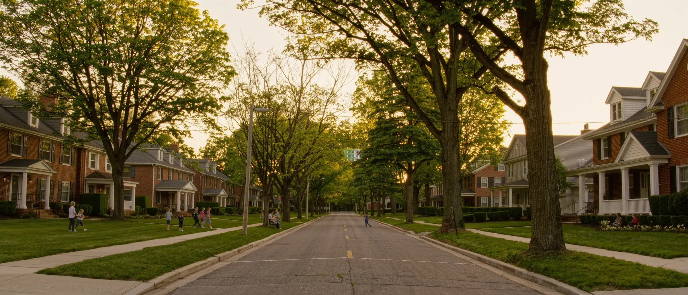 A tree lined suburban street of brick homes at golden hour