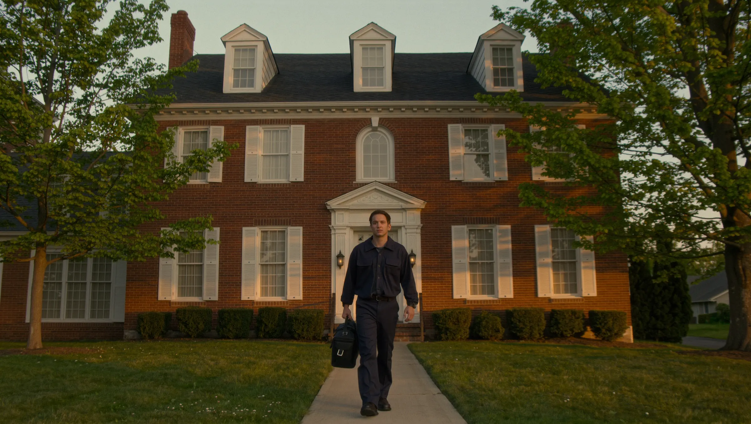 A Keelhouse technician walking up the front path of a brick colonial home at sunset