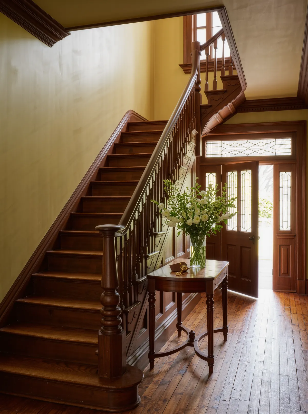 The entry hall of the inn, with a wooden staircase, heart pine floors and flowers on a console table by the open front door