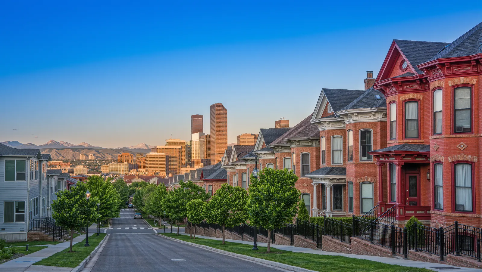 Red brick Victorian homes on a hillside street with the downtown Denver skyline beyond the rooftops