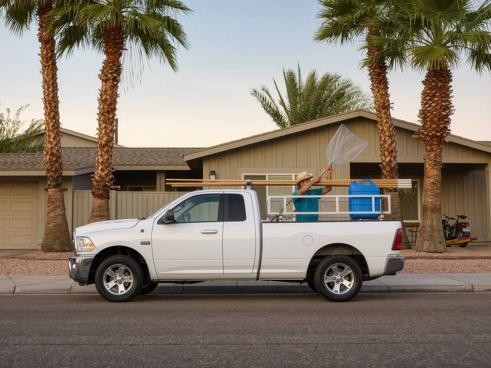 A white service pickup with pool poles, a leaf net and a chemical caddy on a Phoenix street at sunrise