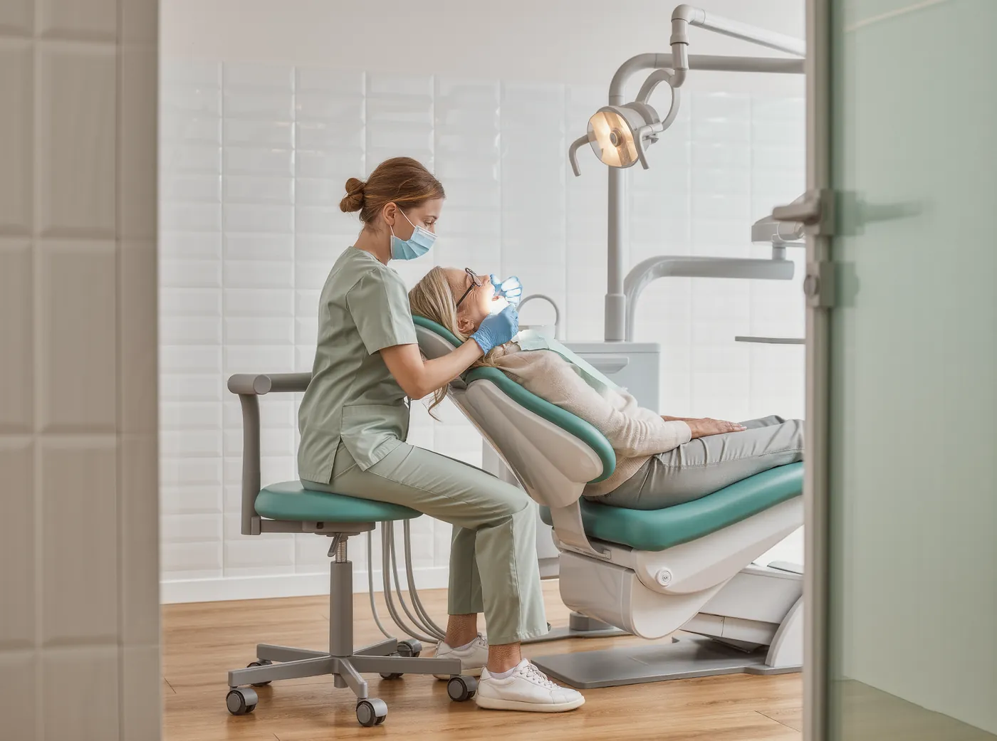 A hygienist cleaning a relaxed patient's teeth in a bright treatment room